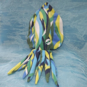 May include: A plush, colorful squid toy with a vibrant pattern of blue, green, yellow, and white. The toy has a rounded head and multiple tentacles, and is made of soft fabric. The background is a light blue.