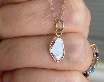 Puede incluir: Un delicado collar de cadena de oro con un colgante que presenta un diamante en bruto, transparente. El diamante está engastado en un bisel de oro y tiene una forma única e irregular.