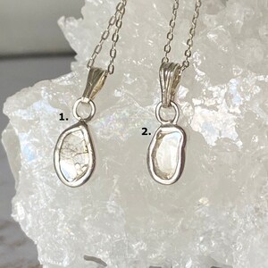 May include: Two silver necklaces with raw diamond pendants. The diamonds are clear and have a rough, natural texture. The necklaces are on a white background.