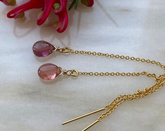 Puede incluir: Un par de pendientes de cadena dorada con piedras preciosas de color rosa en forma de lágrima. Los pendientes tienen un diseño de cadena delicado y están terminados con postes dorados.