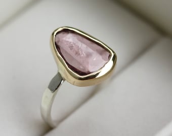 Könnte beinhalten: Ein Ring mit einem rosafarbenen Edelstein, der in einer goldenen Fassung sitzt. Der Ringband ist aus Silber.