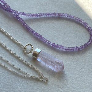 Puede incluir: Dos collares, uno con una cadena de plata y un colgante de cristal morado, y el otro con una cadena delicada de peque&ntilde;as cuentas moradas.