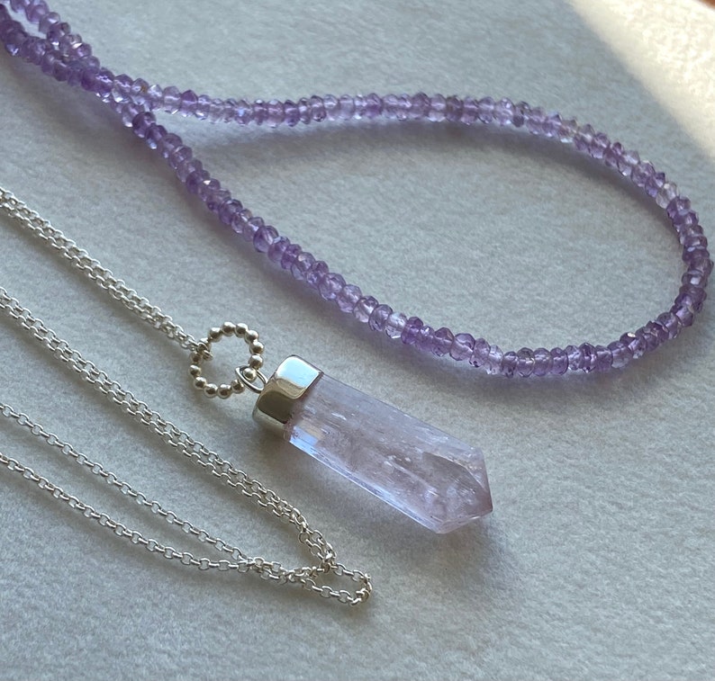 Puede incluir: Dos collares, uno con una cadena de plata y un colgante de cristal morado, y el otro con una cadena delicada de peque&ntilde;as cuentas moradas.