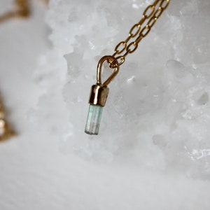 May include: A gold chain necklace with a small, light blue and green crystal pendant.