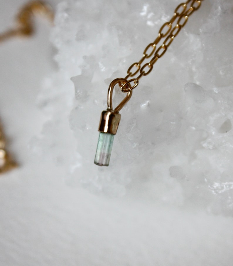 May include: A gold chain necklace with a small, light blue and green crystal pendant.