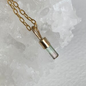 May include: A gold chain necklace with a small, light green and white crystal pendant.