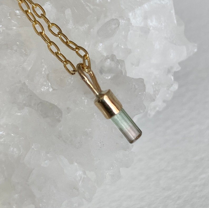 May include: A gold chain necklace with a small, light green and white crystal pendant.