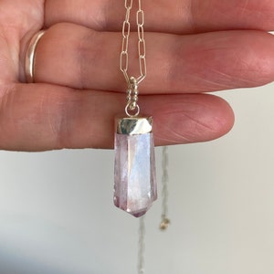 Puede incluir: Un collar de cadena de plata con un colgante de cristal transparente, facetado, de color p&uacute;rpura claro.