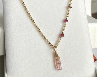 May include: A gold chain necklace with a pink and brown crystal pendant. The chain is adorned with small pink and brown beads.
