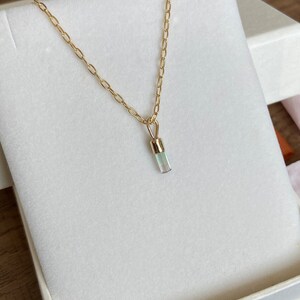 May include: A gold chain necklace with a light blue crystal pendant. The pendant is a long, thin rectangle.