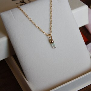 May include: A delicate gold chain necklace with a small, clear, rectangular pendant. The pendant is set in gold and has a subtle shimmer.