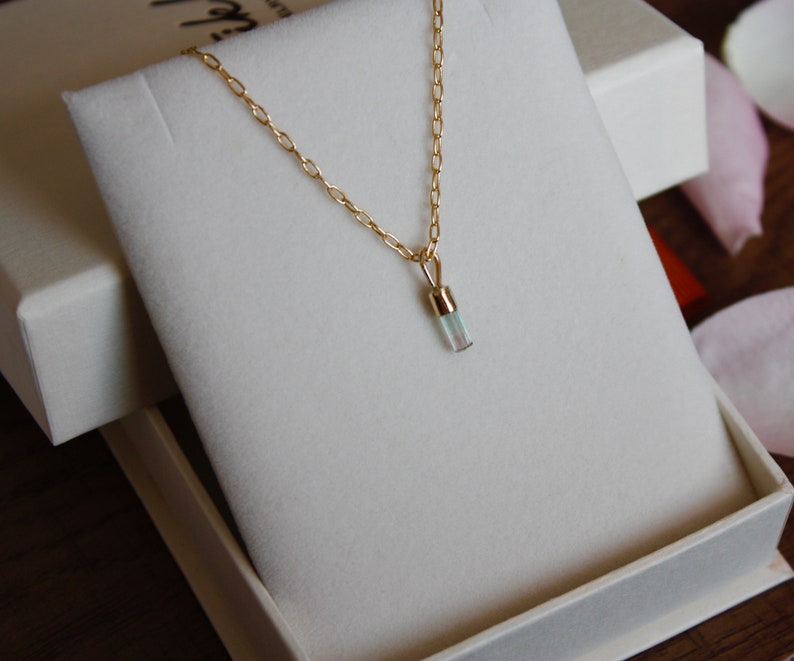 May include: A delicate gold chain necklace with a small, clear, rectangular pendant. The pendant is set in gold and has a subtle shimmer.