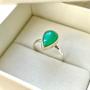 May include: A teardrop-shaped green gemstone ring set in silver. The ring is in a white box.