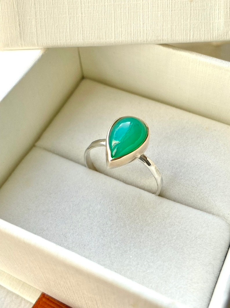 May include: A teardrop-shaped green gemstone ring set in silver. The ring is in a white box.