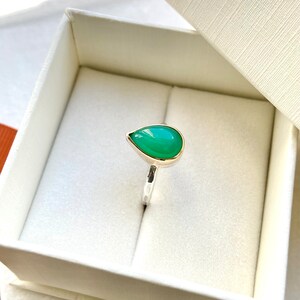 May include: A teardrop-shaped green gemstone ring set in silver with a gold band.