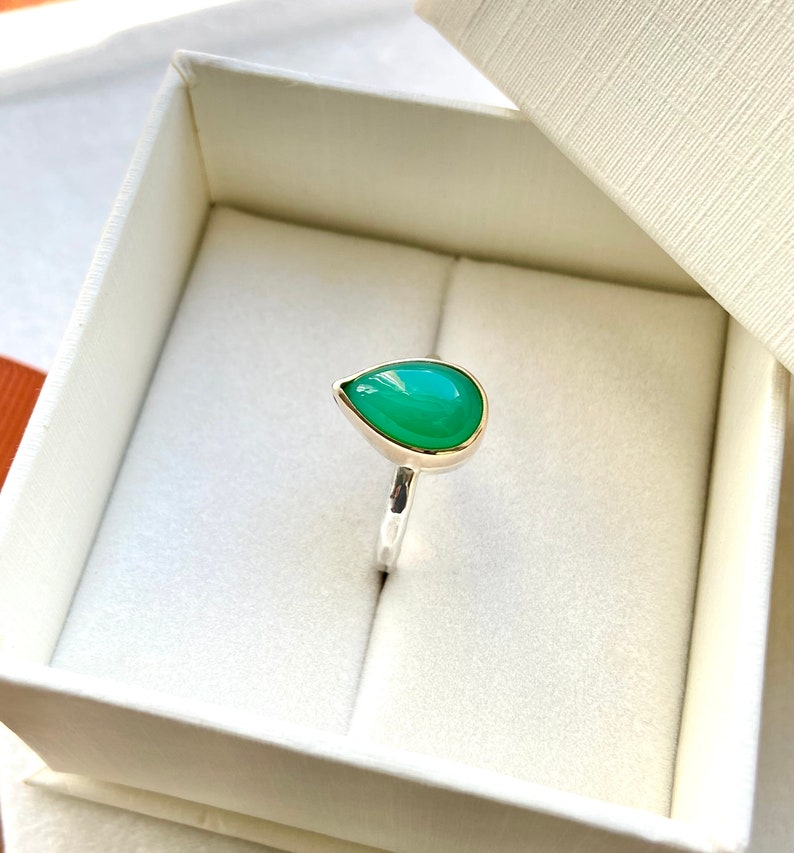 May include: A teardrop-shaped green gemstone ring set in silver with a gold band.