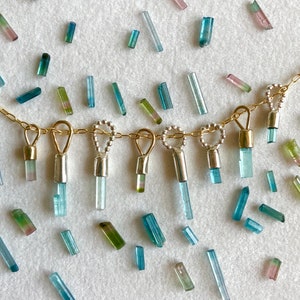 May include: A gold chain necklace with multiple dangling charms featuring small blue, green, and pink tourmaline crystals.