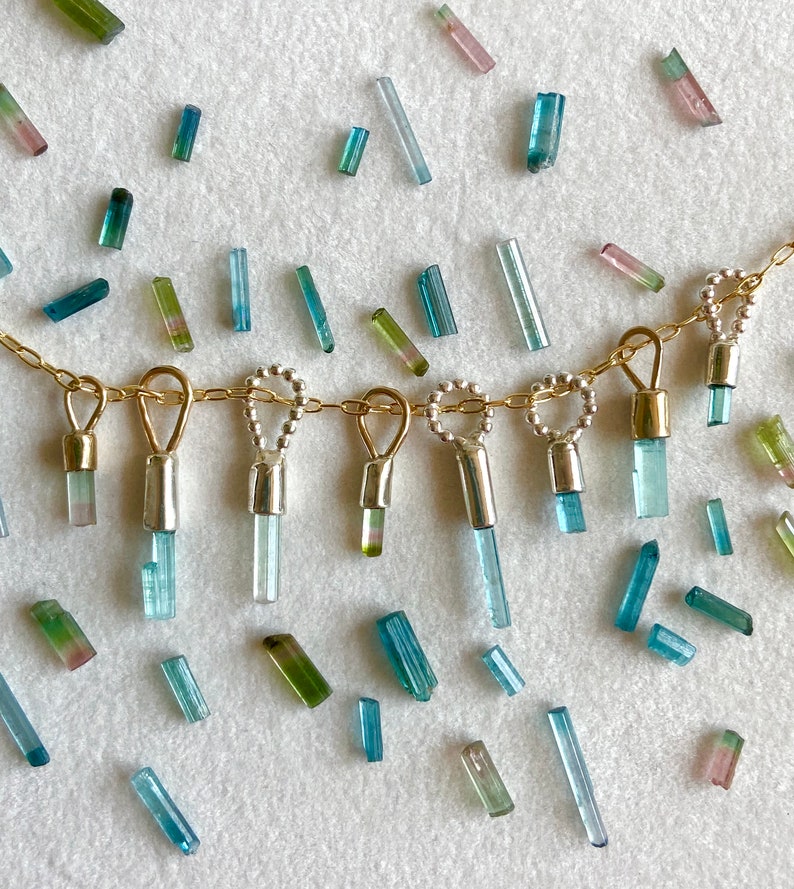 May include: A gold chain necklace with multiple dangling charms featuring small blue, green, and pink tourmaline crystals.