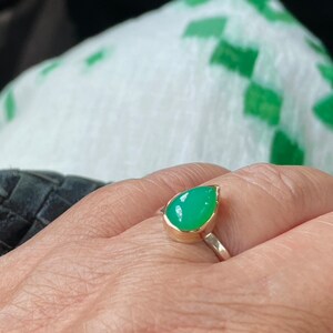 May include: A teardrop-shaped green gemstone ring set in gold and silver.