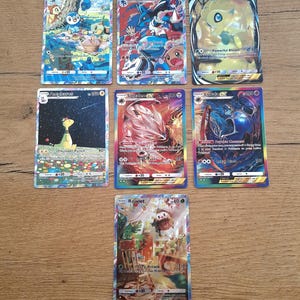 May include: A collection of seven rectangular trading cards featuring colorful illustrations of various creatures. The cards display names such as Piplup, Lucario, Celebi GX, Ampharos, Solgaleo GX, Lunala GX, and Rowlet, along with printed text and game statistics.