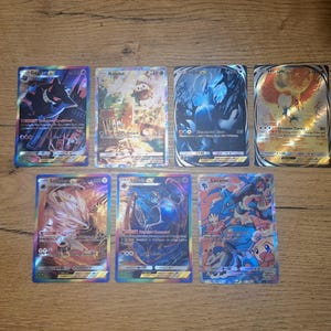May include: Seven rectangular trading cards featuring colorful illustrations of various creatures. The cards include Gengar-EX, Rowlet, Lugia-EX, Ho-Oh-EX, Solgaleo-EX, Lunala-EX, and Lucario. Each card displays specific text, HP values, and holographic foil details.