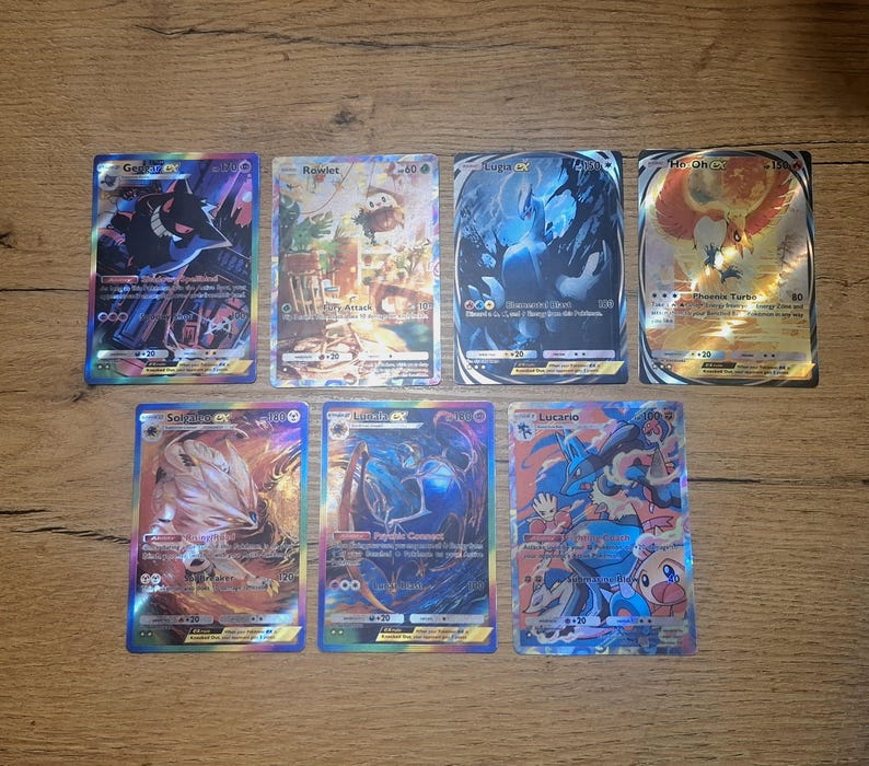 May include: Seven rectangular trading cards featuring colorful illustrations of various creatures. The cards include Gengar-EX, Rowlet, Lugia-EX, Ho-Oh-EX, Solgaleo-EX, Lunala-EX, and Lucario. Each card displays specific text, HP values, and holographic foil details.