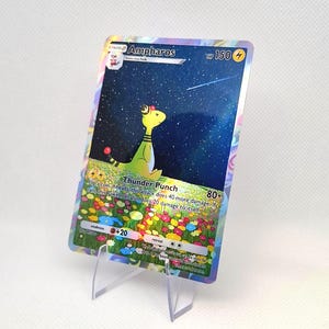 May include: A holographic Ampharos trading card featuring a yellow creature in a field of colorful flowers under a starry night sky. The card displays the name Ampharos, 150 HP, and the Thunder Punch attack text, all set within a reflective border.