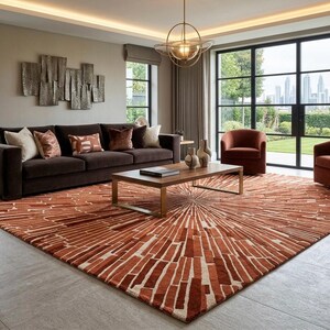 May include: A contemporary living room with a dark brown sofa, two rust-coloured armchairs, and a wooden coffee table. A large rug in shades of rust and cream covers the floor. A large window offers a view of a cityscape. The rug's dimensions are approximately 300cm x 400cm.