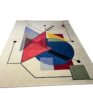 May include: A rectangular rug with a cream background and a geometric design. The design features red, blue, yellow, and green shapes, with black lines and accents. The rug has a modern, abstract aesthetic, suitable for a living space.