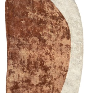 Puede incluir: Alfombra abstracta con una forma &uacute;nica, que presenta una mezcla de tonos marrones y beige. La alfombra tiene una apariencia texturizada y afelpada, con un tacto suave y aterciopelado. El dise&ntilde;o es moderno y complementar&iacute;a varios estilos de interior.