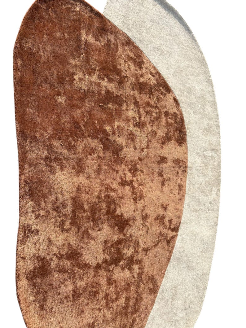 Puede incluir: Alfombra abstracta con una forma &uacute;nica, que presenta una mezcla de tonos marrones y beige. La alfombra tiene una apariencia texturizada y afelpada, con un tacto suave y aterciopelado. El dise&ntilde;o es moderno y complementar&iacute;a varios estilos de interior.