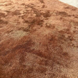 Puede incluir: Primer plano de una alfombra de felpa texturizada en tonos marrones y beige. La alfombra tiene un pelo denso, creando una apariencia suave y acogedora. Las variaciones de color a&ntilde;aden profundidad e inter&eacute;s visual al revestimiento del suelo.