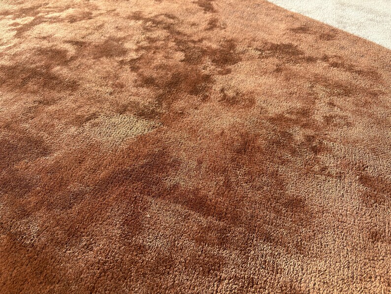 Puede incluir: Primer plano de una alfombra de felpa texturizada en tonos marrones y beige. La alfombra tiene un pelo denso, creando una apariencia suave y acogedora. Las variaciones de color a&ntilde;aden profundidad e inter&eacute;s visual al revestimiento del suelo.