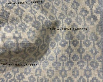 May include: Close-up of a light blue and white patterned textile. The design features repeating geometric shapes and floral motifs. The text "THE ANCIENT CARPETS" is printed across the image. The textile appears to be soft and textured.