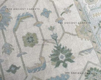 Könnte beinhalten: Nahaufnahme eines beigefarbenen Teppichs mit einem detaillierten Blumenmuster in Blau-, Grün- und Beigetönen. Der Text "THE ANCIENT CARPETS" wiederholt sich auf der Oberfläche des Teppichs. Der Teppich hat eine strukturierte Optik.