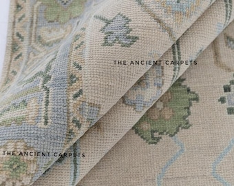 Könnte beinhalten: Beige und blauer Teppich mit floralem Muster und Used-Look. Der Teppich trägt den Text "THE ANCIENT CARPETS". Der Teppich ist gefaltet und zeigt seine Textur und sein Muster. Die Farben sind gedämpft.