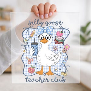 May include: A square clear acrylic sheet featuring a cartoon white goose wearing glasses and a blue floral bow. The text reads silly goose teacher club. Surrounding the goose are school supplies including a pencil, books, an apple, and a ruler.