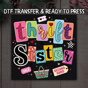 May include: A colorful graphic design on a black background with the words "Thrift Sister" in large, playful letters. The design includes various elements like hearts, stars, and a shopping basket, with the text "DTF TRANSFER & READY TO PRESS" at the top.