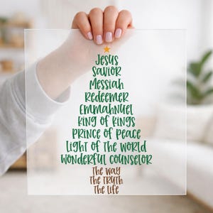 May include: A square, frosted acrylic sign featuring a Christmas tree shape formed by green text that reads Jesus, Savior, Messiah, Redeemer, Emmanuel, King of Kings, Prince of Peace, Light of the World, Wonderful Counselor, and brown text The Way, The Truth, The Life.