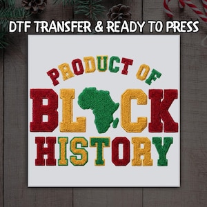 May include: A white square canvas with the words "PRODUCT OF BLACK HISTORY" in a varsity-style font. The text is in red, yellow, and green, with a green outline of the African continent in the center. The words "DTF TRANSFER & READY TO PRESS" are at the top.