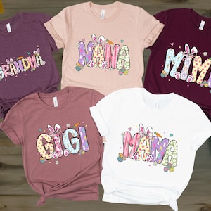May include: Five short-sleeved t-shirts in various colors, each featuring a different Easter-themed graphic. The shirts display the words "Grandma," "Nana," "Mimi," "Gigi," and "Mama" in colorful, playful fonts with bunny ears and Easter egg accents.