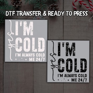 May include: Two gray DTF transfer designs with the text "I'M COLD I'M ALWAYS COLD ME 24/7". One design has white text, the other has black text. The phrase "DTF TRANSFER & READY TO PRESS" is at the top.