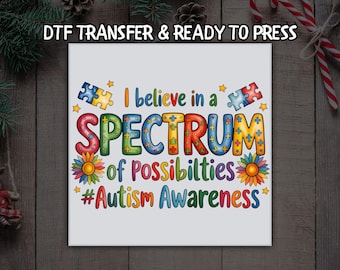 May include: A white DTF transfer with the text "I believe in a SPECTRUM of Possibilities #Autism Awareness" in colorful letters. The design includes puzzle pieces, stars, and flowers, ready to press.