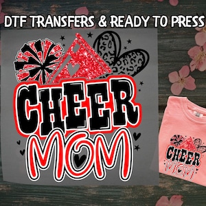 May include: A DTF transfer design with the words "CHEER MOM" in a bold, black and red font. The design includes a pom-pom, a glittery red triangle, and a leopard print heart. A pink t-shirt with the same design is also shown.