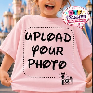 May include: A light pink t-shirt with the words "UPLOAD YOUR PHOTO" in black script. A camera icon is below the text. The shirt also has a "DTF TRANSFER READY TO PRESS" graphic.