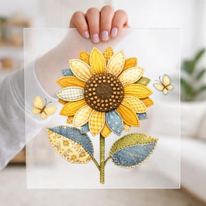 May include: A decorative sunflower design with yellow, blue, and green fabric petals and leaves. The sunflower has a brown center and is accompanied by two butterfly illustrations. The design is held up by a person.