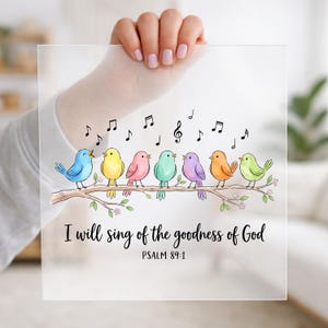 May include: A square frosted acrylic sign featuring a colorful illustration of seven small birds perched on a brown branch with musical notes above them. The text reads, "I will sing of the goodness of God" followed by "PSALM 89:1" in black script.