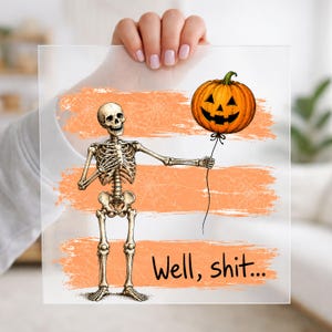 May include: A square acrylic sign featuring a skeleton illustration holding a string attached to a jack-o'-lantern balloon. The background has orange brush strokes with a spiderweb pattern. The text "Well, shit..." is printed in black at the bottom.
