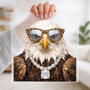 May include: A square print featuring a detailed painting of a bald eagle wearing leopard print glasses and a silver-toned chain necklace with a large, square-cut clear gemstone pendant. The eagle has white head feathers and brown body feathers.
