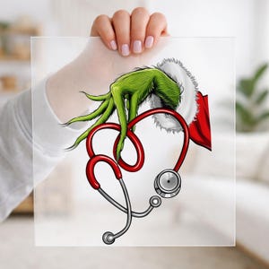May include: A graphic illustration featuring a green, furry hand with long fingers emerging from a red and white fur-trimmed sleeve, holding a red stethoscope shaped into a heart outline. The design is printed on a square, transparent sheet.